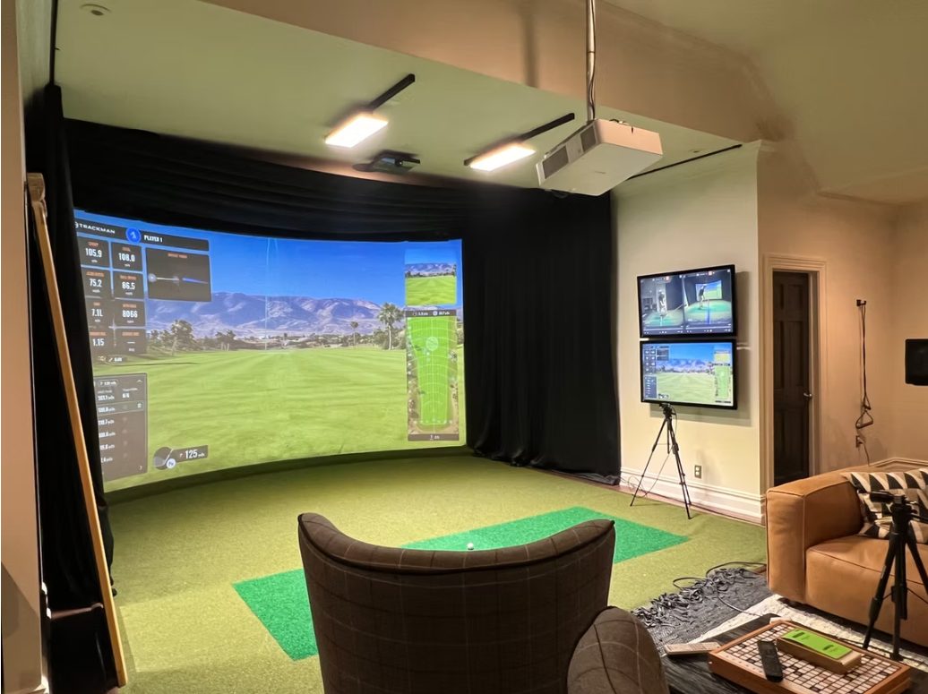 Completed golf simulator installation by the ynVISION team — enclosed hitting bay with curved impact screen, ceiling-mounted projection, turf hitting strips and secondary displays Completed enclosed golf simulator room installed by ynVISION